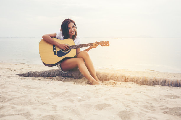 亚洲年轻女子在海滩上弹吉他图片下载