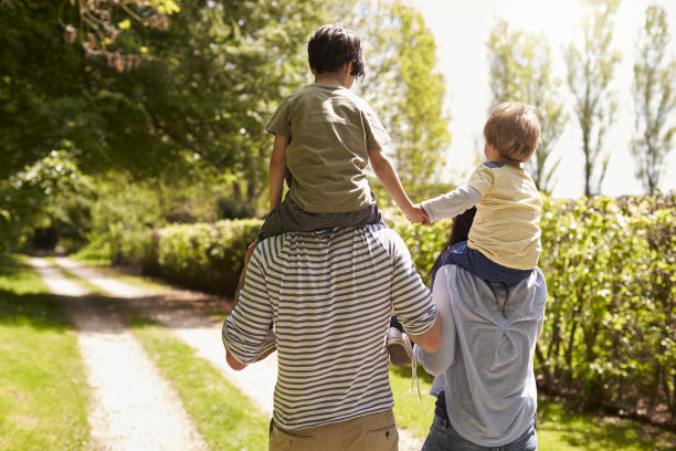 父母让儿子骑在肩膀上走路的后视图图片下载