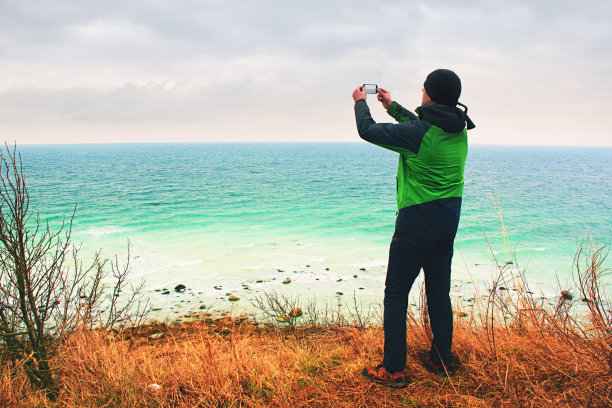 穿着防水夹克的男人用智能手机拍下海岸的照片图片下载