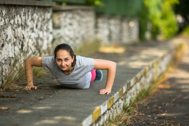 年轻的运动女性在公园里做俯卧撑。图片下载