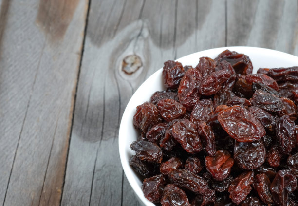 白杯里的葡萄干放在木地板上。素材图片