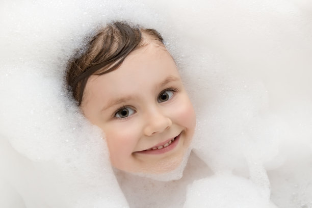 漂亮的微笑小女孩正在用肥皂泡沫洗澡图片下载
