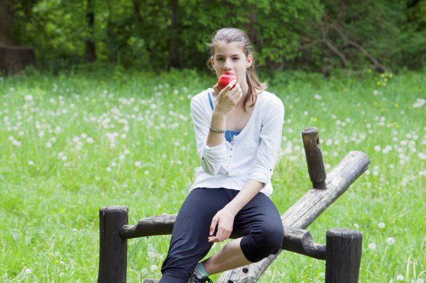 年轻女子坐在跷跷板上吃东西图片下载
