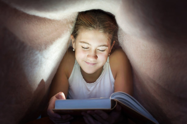 年轻开朗的少女躲在毯子下面看书图片下载