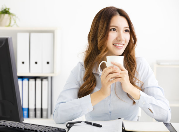 年轻的女商人一边喝咖啡一边看图片下载