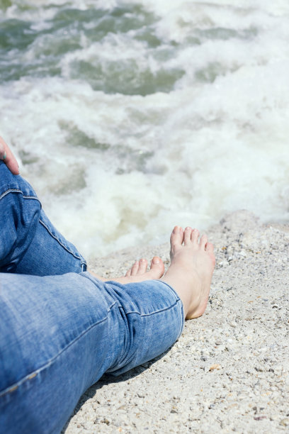 赤脚女人穿着牛仔裤坐在岸边图片下载