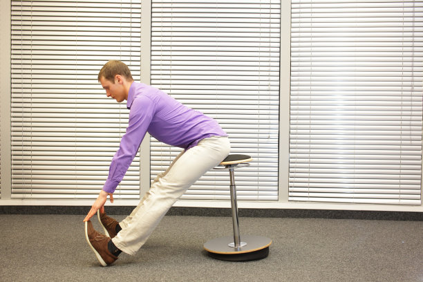 在办公室里，一个男人在充气凳子上用手摸着脚趾练习图片下载