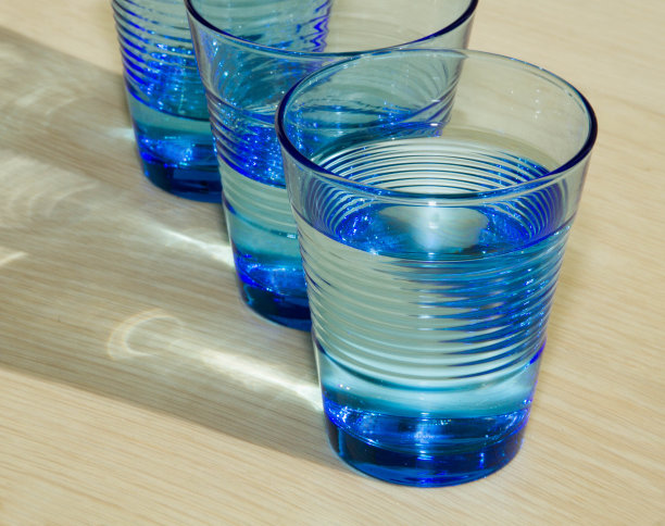 三杯蓝色的水在米黄色的木头背景上图片下载