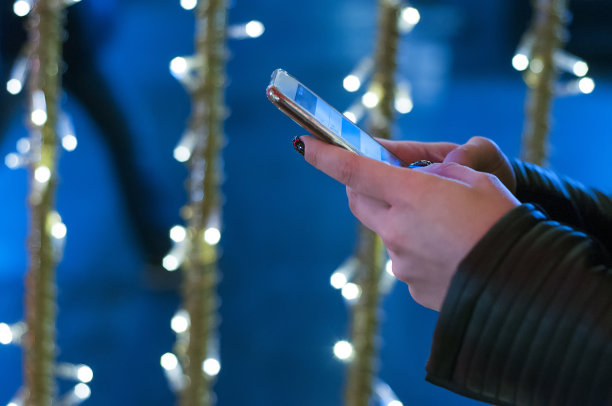 女人拿着智能手机在背景发光散景圣诞照明图片下载