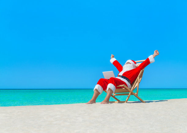 圣诞老人喜欢在海滩的躺椅上使用笔记本电脑工作图片下载