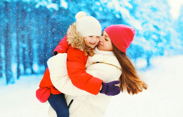 冬天快乐的微笑母亲拥抱亲吻孩子的雪花图片下载