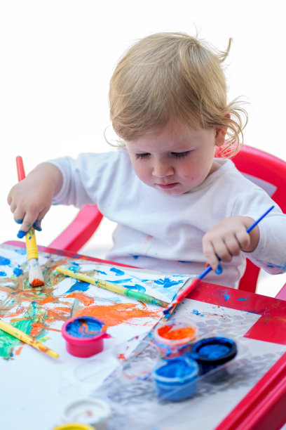 可爱的小男孩用画笔在纸上涂色。素材图片