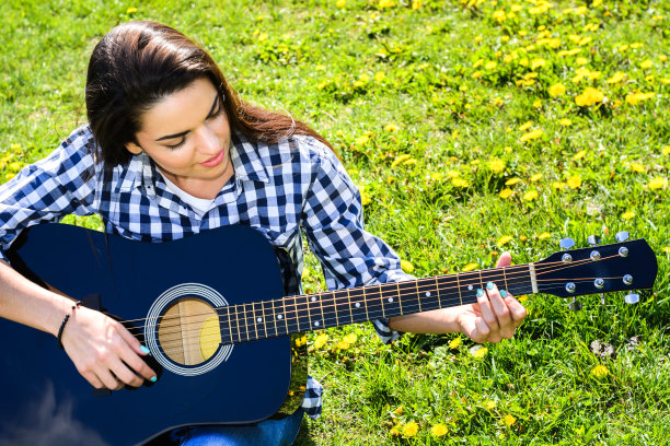 女孩在绿色的草地上弹吉他图片下载