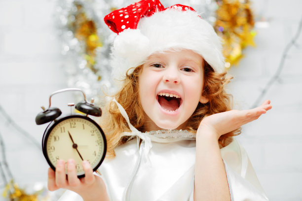 快乐的小女孩戴着圣诞帽，拿着一个时钟。图片下载