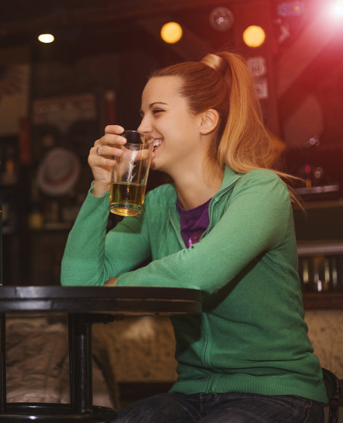 坐在酒吧里喝啤酒的快乐女人。图片下载
