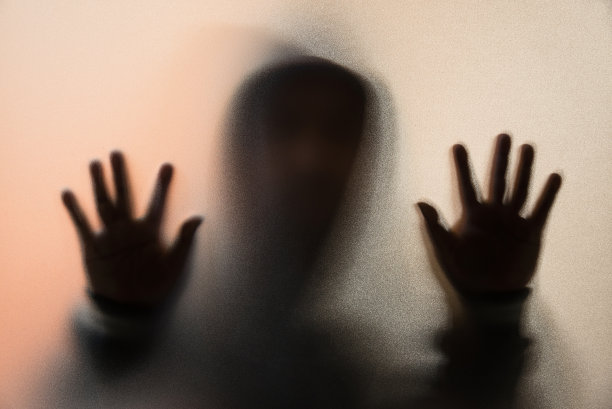 阴影模糊的恐怖的人夹克和兜帽。把手放在玻璃上。磨砂玻璃后面的危险人物。神秘人。万圣节的背景。模糊的照片图片下载