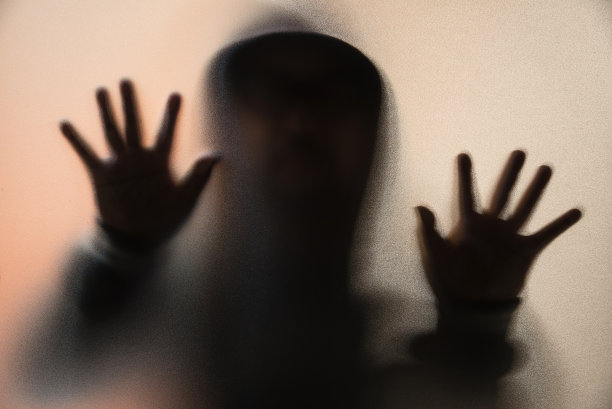 阴影模糊的恐怖的人夹克和兜帽。把手放在玻璃上。磨砂玻璃后面的危险人物。神秘人。万圣节的背景。模糊的照片图片下载