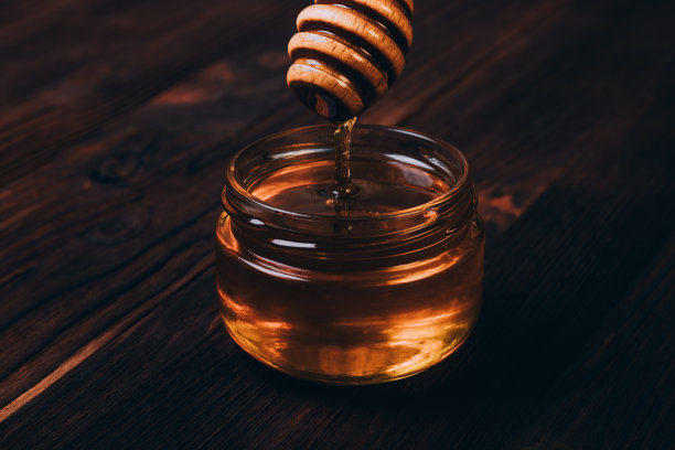 蜂蜜滴进桌子上的罐子里素材图片