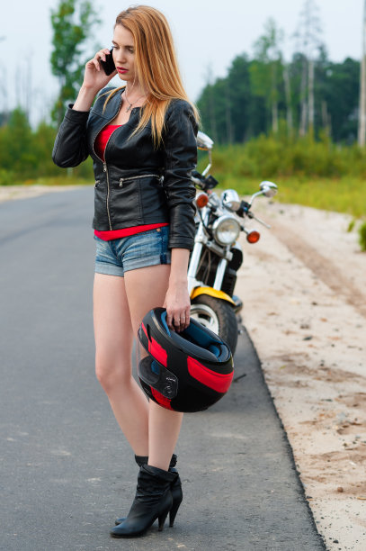 骑摩托车的年轻女子一边拿着摩托车头盔一边打电话图片下载