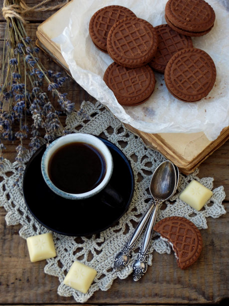巧克力曲奇与白奶油，一杯咖啡和一束薰衣草木制背景的浪漫组合。有选择性的重点。图片下载