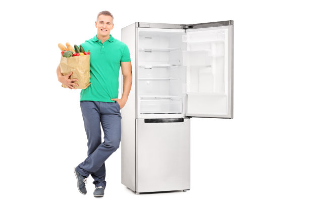 一个拿着购物袋的男人站在空冰箱旁图片下载