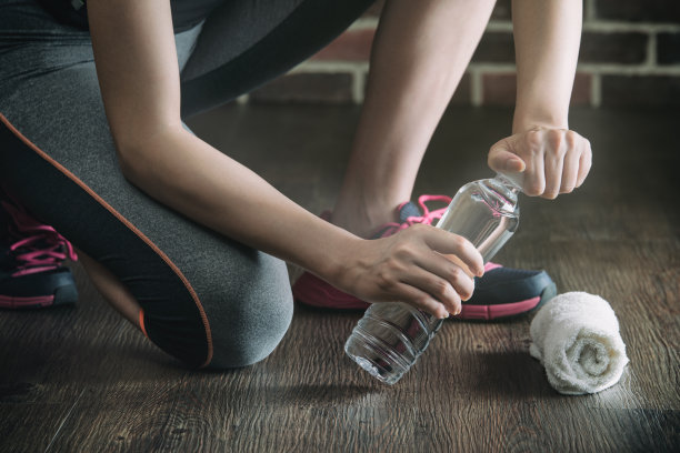 蹲在木地板上休息喝水，健身锻炼图片下载