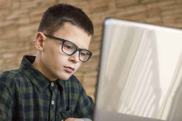 戴眼镜的男孩坐在桌子上使用笔记本电脑图片下载