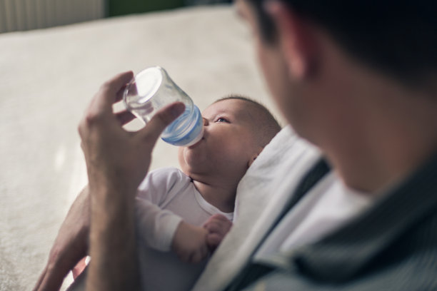 一个父亲给一个可爱的婴儿喂奶的特写素材图片