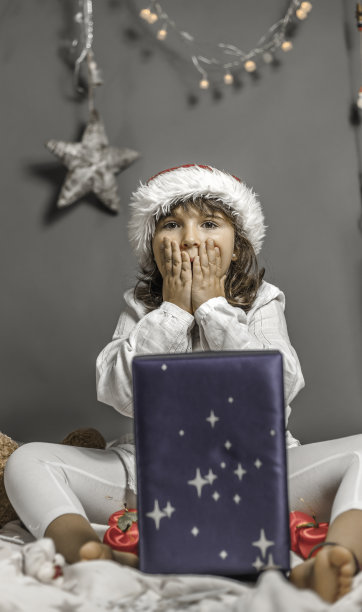 美丽的女孩戴着圣诞老人的帽子惊喜地打开了一份礼物。圣诞节图片下载
