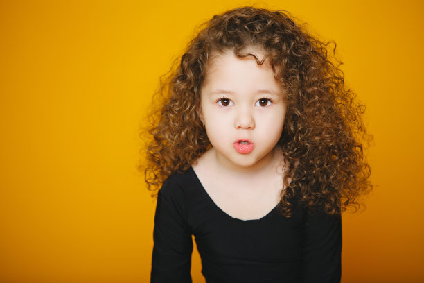 小卷毛女孩亲吻在工作室在橙色的背景。复制图片下载