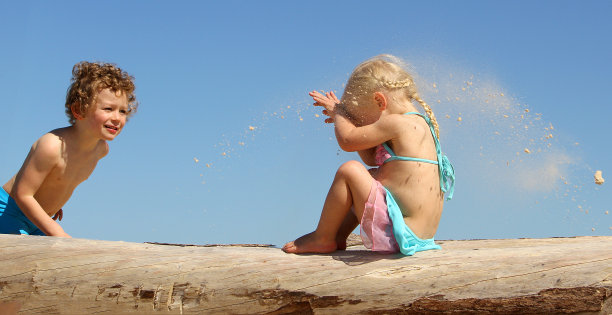 小男孩在沙滩上向小女孩扔沙子图片下载