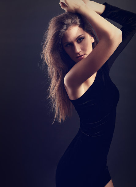 性感自然的身材苗条的模特在黑色的裙子在深灰色的背景下摆姿势，手臂高于头部。健美的特写肖像图片下载