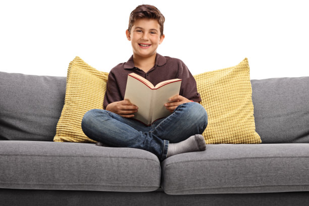 快乐的男孩坐在沙发上拿着一本书图片下载