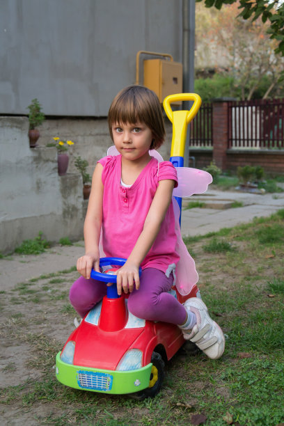 有蝴蝶翅膀的小女孩在汽车玩具里玩得很开心图片下载
