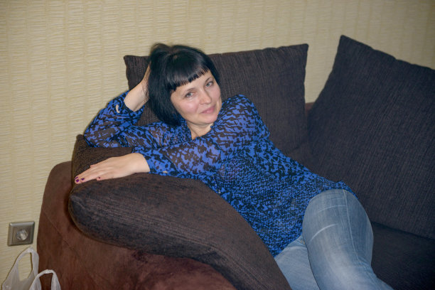 穿着牛仔裤和衬衫的成熟女人在沙发上摆姿势。图片下载