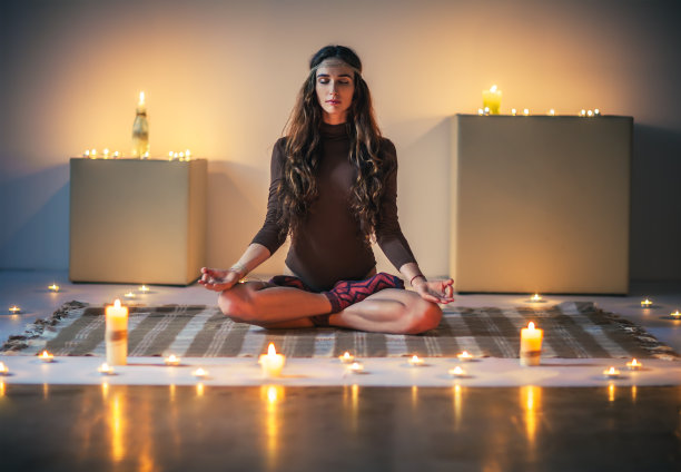 年轻美丽的女人沉思莲花姿势在舒适的房间与蜡烛图片下载