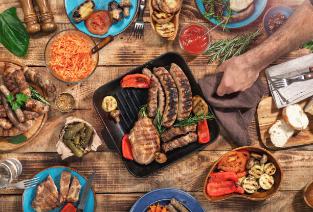 木桌上有不同的食物，烤牛排、香肠和烤蔬菜，俯视图素材图片