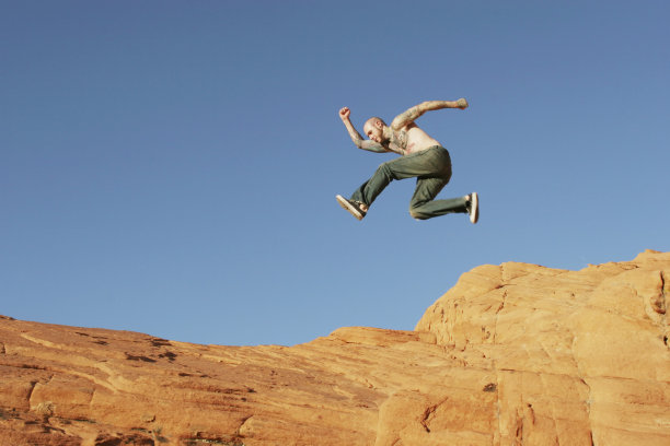 男人在红色的岩石上跳图片下载