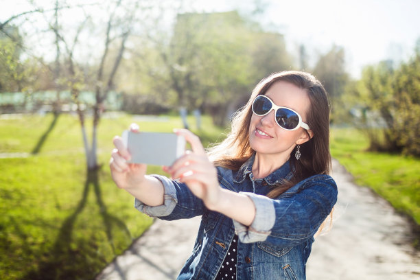 年轻女孩戴着太阳镜用智能手机自拍图片下载