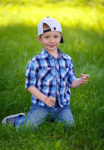 小男孩正坐在公园的绿草地上图片下载