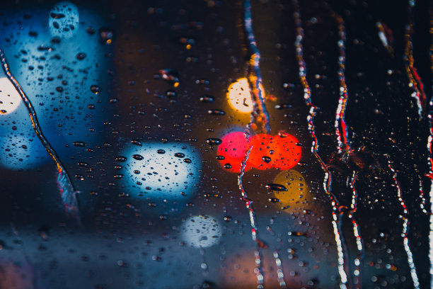 雨点落在汽车挡风玻璃上，路面灯光变得模糊图片下载