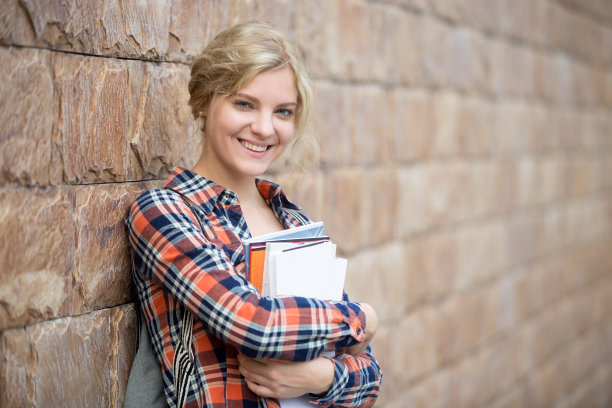 一个拿着书靠在砖墙上的学生的肖像图片下载