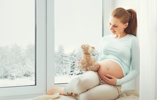 一个快乐的孕妇坐在冬天的窗口图片下载