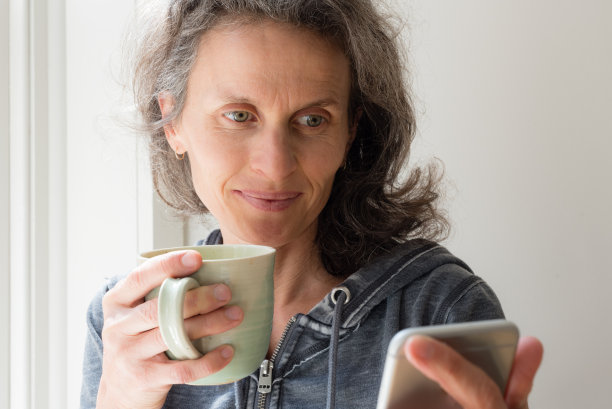 拿着绿色杯子和手机的中年妇女图片下载