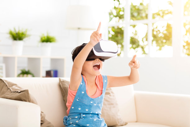 快乐的小女孩戴着虚拟现实头盔坐在沙发上图片下载