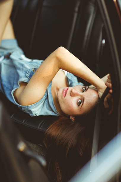 女孩躺在汽车的皮座椅上。彩色照片图片下载