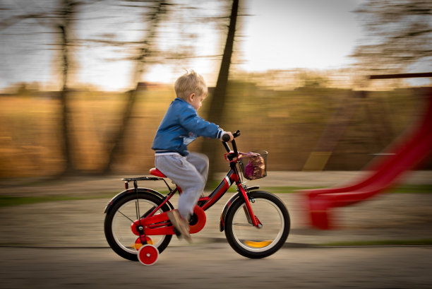 一个小男孩骑着自行车，没戴头盔，在公园里。图片下载