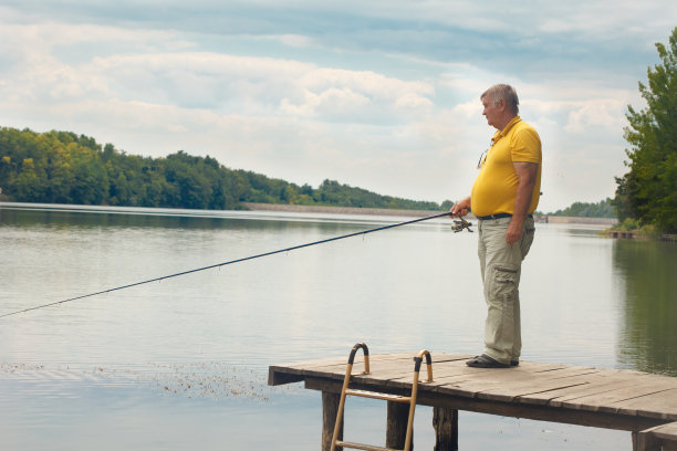 老人站在木制码头上钓鱼图片下载