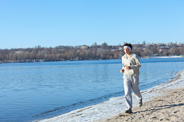 女性跑步者在冬季河岸上跑步。图片下载