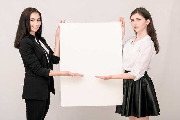 两个快乐地微笑着的年轻商业妇女拿着一个大的空白招牌图片下载